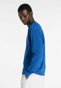 T-shirt blu a maniche lunghe in cotone, con collo rotondo e polsini a coste, dal taglio rilassato e dotato di tasche laterali.