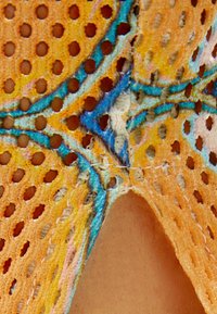 Orange nättextil med stora hål, med blå och gula accenter. Strukturerad yta med synlig sömnadsdetalj och fransade kanter.