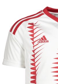 Witte sporttrui met rode driehoekige patronen, rode strepen op de schouders en een geborduurd rood Adidas-logo.