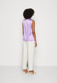 Top sin mangas de color púrpura claro en tejido de satén, combinado con pantalones de pierna ancha en color crema. Textura suave y ligero brillo, con un detalle de costura en la parte trasera.