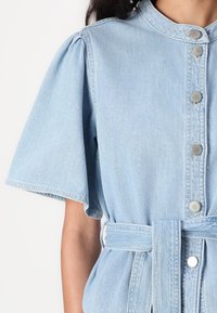 Light blue denim dress with short puff sleeves, a button-down front, a collar, and a fabric belt at the waist. Smooth texture and subtle stitching.