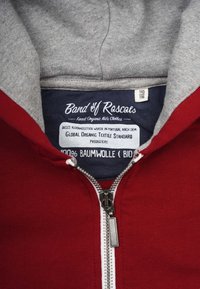 Red zip-up hoodie with gray lining, featuring a silver zipper and tag stating "100% Baumwolle," indicating organic cotton material.