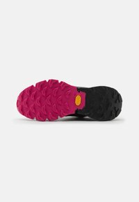 Črna in roza podplat tekaških čevljev za terensko tek s trdim profilom. Vsebuje logo Vibram in teksturirano površino za boljši oprijem.