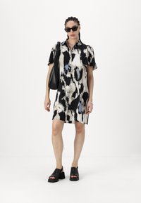 Rochie cu mânecă scurtă, cu un model abstract alb-negru și accente albastre, cu închidere cu nasturi în față și croială lejeră. Asortată cu pantofi cu talpă înaltă negri.