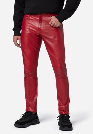 Rote Lederhosen im Slim-Fit-Stil, mit glatter Textur und kontrastierenden Nähten, kombiniert mit schwarzen Sneakers.