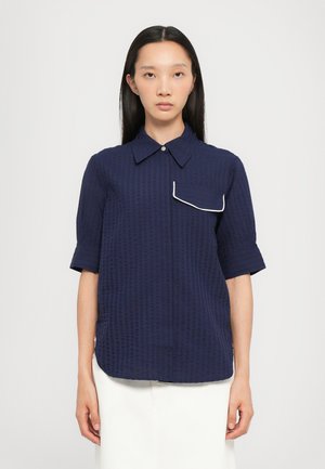 Navy blue short-sleeve shirt with a textured pattern, a pointed collar, and a white piped pocket detail on the left chest.