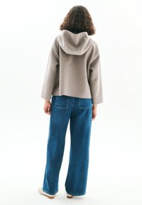 Sweater gris à capuche, court, avec des manches larges, associé à un jean bleu en denim taille haute, droit, avec poches arrière et coutures légères.
