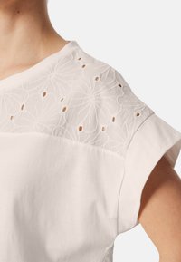 Vit bomullsskorta med en detaljerad broderad axelklapp med utskurna mönster, uppvikta ärmar och en avslappnad passform.