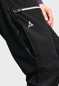 Schwarze Hose mit einer seitlichen Reißverschlusstasche aus Mesh, einem grauen Reißverschluss und einem weißen Logo-Akzent in der Nähe der Tasche, aus einem glatten Stoff gefertigt.