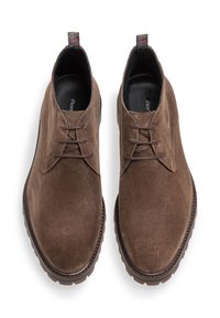 Zapatos de ante marrón con una textura suave, que presentan un diseño de cordones, detalles de costura, una puntera redondeada y una etiqueta en el talón con un patrón.