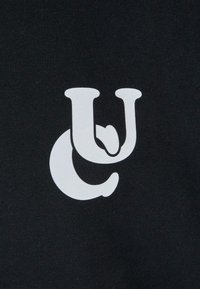 Melnas audums ar lielu baltu grafiku, kas apvieno burtus "U" un "C". Tekstūra izskatās gluda un nedaudz elastīga.