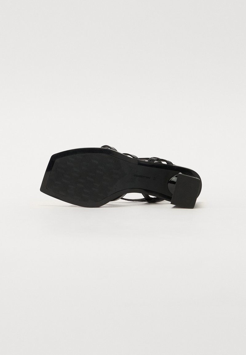 Sandale noire à talons hauts avec une semelle texturée et des brides de cheville. Le talon est en forme de bloc, offrant stabilité et soutien.