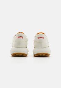 Vita sneakers med röd "CAMPER"-branding, orange detaljer, slät textur, rund form och en gummisul med cirkulära grepp.