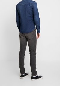 Mörkblå denimskjorta med en ok-design, kombinerad med grå jeans och svarta sneakers. Tyget har en jämn struktur och en figurformad silhuett.