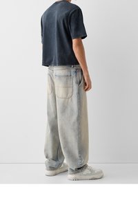 Överdimensionerad navy bomulls T-shirt med korta ärmar, som kombineras med ljusblå säckiga denimjeans. Har två bakfickor och blekta detaljer.