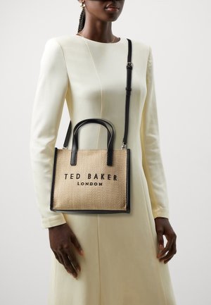 Beżowa pleciona torba z czarnymi akcentami, wyposażona w dwa krótkie uchwyty i odpinany pasek, z napisem "TED BAKER LONDON" dużymi literami.