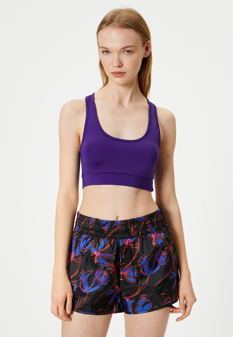 Lilla cropped sports top med rund halsudskæring, parret med sorte shorts med et farverigt blomsterprint og elastisk talje.