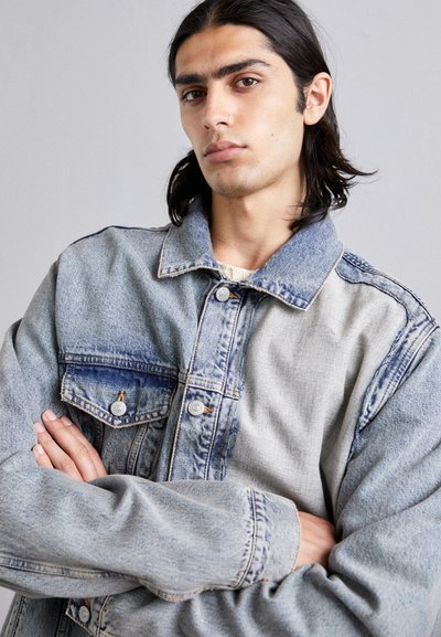 Denim jacket featuring a two-tone design with light blue on one side and darker blue accents, finished with silver buttons and a relaxed fit.