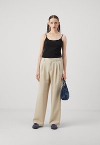 Black spaghetti strap top, cream wide-leg trousers, and a textured blue handbag. Footwear features a rounded design in shades of grey.