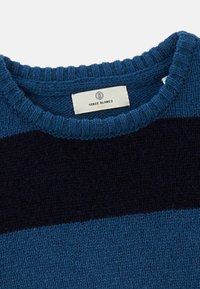 Pull en tricot marine et deux teintes de bleu, avec un col côtelé et une étiquette portant la mention "Serge Blanco" au niveau du col.