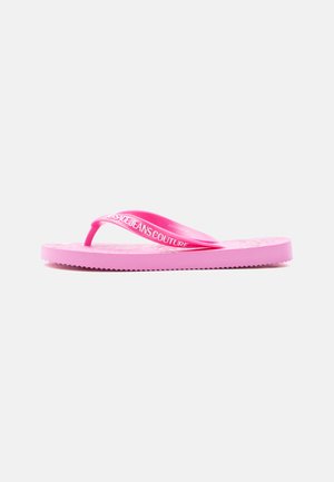 Roze teenslipper met gestructureerde zool en merkriem met de tekst "Versace Jeans Couture" op een witte achtergrond, zijaanzicht.
