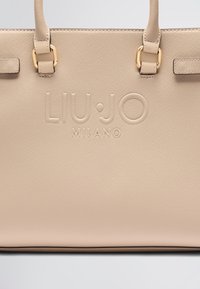 Sac Liu Jo Milano beige avec logo en relief, texture lisse, poignées assorties et accents en métal doré.