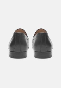 Chaussures en cuir noir avec une texture lisse, dotées d'un bout arrondi et de détails de piqûre subtils, reposant sur un petit talon.