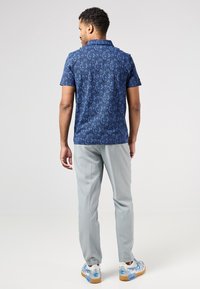 Camisa polo de mangas cortas en color navy con un patrón floral, combinada con pantalones grises claros y zapatillas con estampado y detalles en azul.