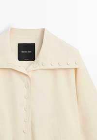 Roomkleurig beige overhemd met kraag en knoopdetails aan de voorkant en schouders, met een zwart Massimo Dutti-label aan de binnenkant van de halslijn.