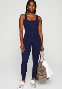 Navy activewear unitard with a square neck, smooth texture, and form-fitting design. Accompanied by a beige bag and white towel.