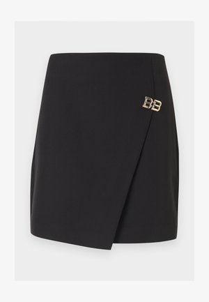 Melna mini svārki ar asimetrisku priekšējo pārklājumu un mazu zelta dekoratīvu BB logotipa piespraudi labajā pusē.