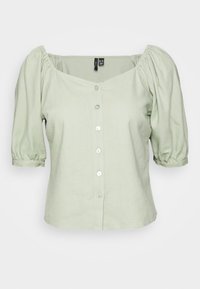 Blouse à manches bouffantes de couleur vert clair avec un décolleté carré et une fermeture à boutons sur le devant. Fabriquée en tissu doux, elle présente cinq boutons ronds le long du centre.