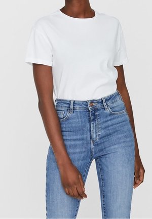 Weißes Baumwoll-T-Shirt mit rundem Ausschnitt, kurzen Ärmeln und lockerer Passform, kombiniert mit hochtaillierten blauen Jeans aus Denim mit Knopfverschluss.