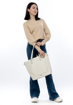Sac fourre-tout en cuir blanc avec doubles poignées, présentant un design minimaliste et des détails de couture subtils, tenu par une personne en tenue décontractée.
