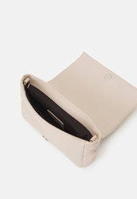 Beige quiltet lædertaske med en glat finish, en magnetisk trykknaplukning og et mørkt stofinteriør. Kompakt design med minimal hardware.