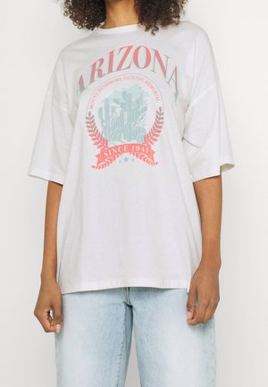 Camiseta blanca de gran tamaño con un estampado gráfico que presenta "ARIZONA", cactus y "DESDE 1941" en colores rojo y teal. Mangas cortas, textura suave.