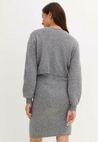 Robe tricotée grise avec un haut de pull court, manches longues et une silhouette ajustée. Texture douce avec des poignets et un ourlet côtelés.