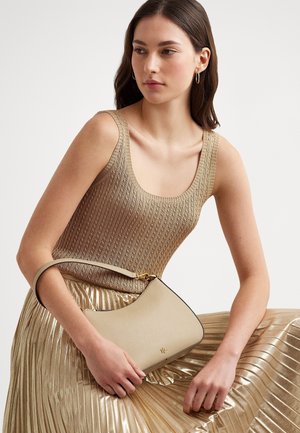 Joven mujer con top de punto beige y falda plisada metálica, sosteniendo un pequeño bolso beige con adornos dorados.