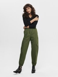 Pantalones cargo verdes con puños elásticos, combinados con una camiseta ajustada de manga larga negra y botas negras hasta el tobillo con acentos metálicos.
