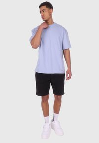 Lys blå kortærmet t-shirt med en afslappet pasform, parret med sorte shorts. Har hvide sneakers og mønstrede hvide sokker.