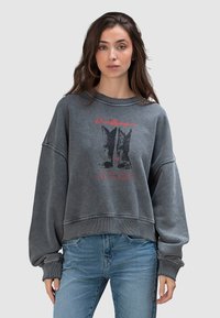 Szara bawełniana bluza dresowa o luźnym kroju, opuszczonych ramionach oraz nadruku graficznym przedstawiającym kowbojskie buty z czerwonym napisem z przodu.