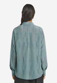 Ljusblå blus med vertikala strukturerade mönster. Långa ärmar, knappmanschetter och klassisk krage. Slätt, flödande tyg.