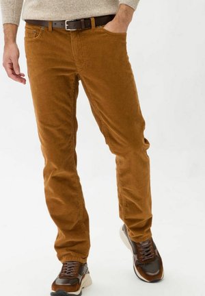 Pantalones de pana marrón con corte recto, con acanaladuras verticales y un cinturón de piel marrón. Llevados con zapatillas marrón y beige.