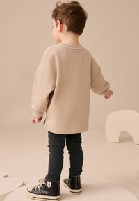 Beige oversize sweatshirt med ribbad mudd, i kombination med mörka ribbade leggings och svarta högskurna sneakers, stående på en ljus yta.