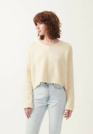 Cream-colored cropped sweater with a V-neck, ribbed cuffs, and soft texture, paired with light blue jeans.