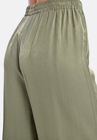 Pantaloni a gamba larga di un verde oliva chiaro con una texture liscia e lucida, caratterizzati da pieghe e una vita elastica per il massimo comfort.