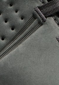 Grauer Schuhobermaterial aus strukturiertem Material, mit Perforationen, einem Reißverschluss und einem kontrastierenden gerippten Akzent.