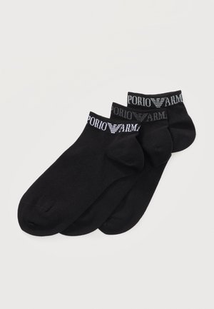 Három pár fekete bokazokni, fehér "Emporio Armani" logóval a szegélyeken, egymáson átfedésben rendezve fehér háttéren.