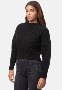Svart kortärmad tröja med en strukturerad stickad mönster, ribbad halsringning och ärmslut, kombinerad med mörka jeans. Lådan passform framhäver en modern stil.