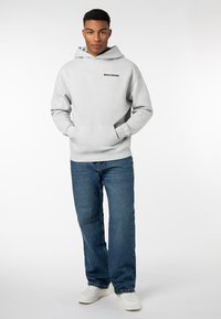 Grauer Hoodie mit einer vorderen Tasche und schwarzem "WORLDWIDE"-Schriftzug, kombiniert mit blauen geraden Jeans und weißen Sneakers. Schlichtes Design, lässige Passform.